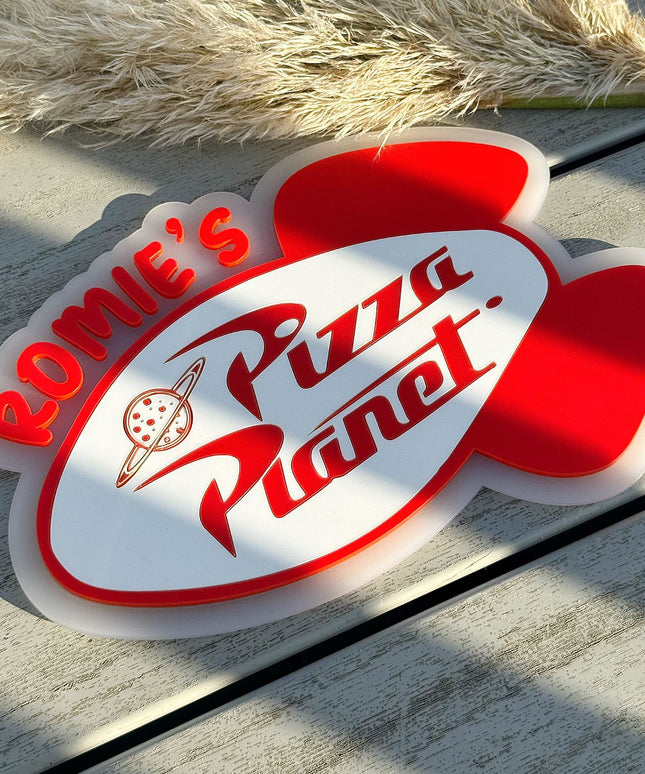 Personalised Pizza Planet wall sign on a wooden surface with pampas grass.