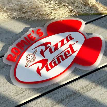 Personalised Pizza Planet wall sign on a wooden surface with pampas grass.
