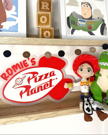 Shelf with 'Rommie's Pizza Planet' sign, toy figures, and framed pictures of cartoon characters.