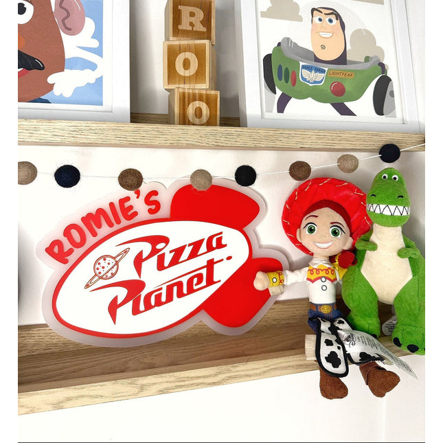 Shelf with 'Rommie's Pizza Planet' sign, toy figures, and framed pictures of cartoon characters.