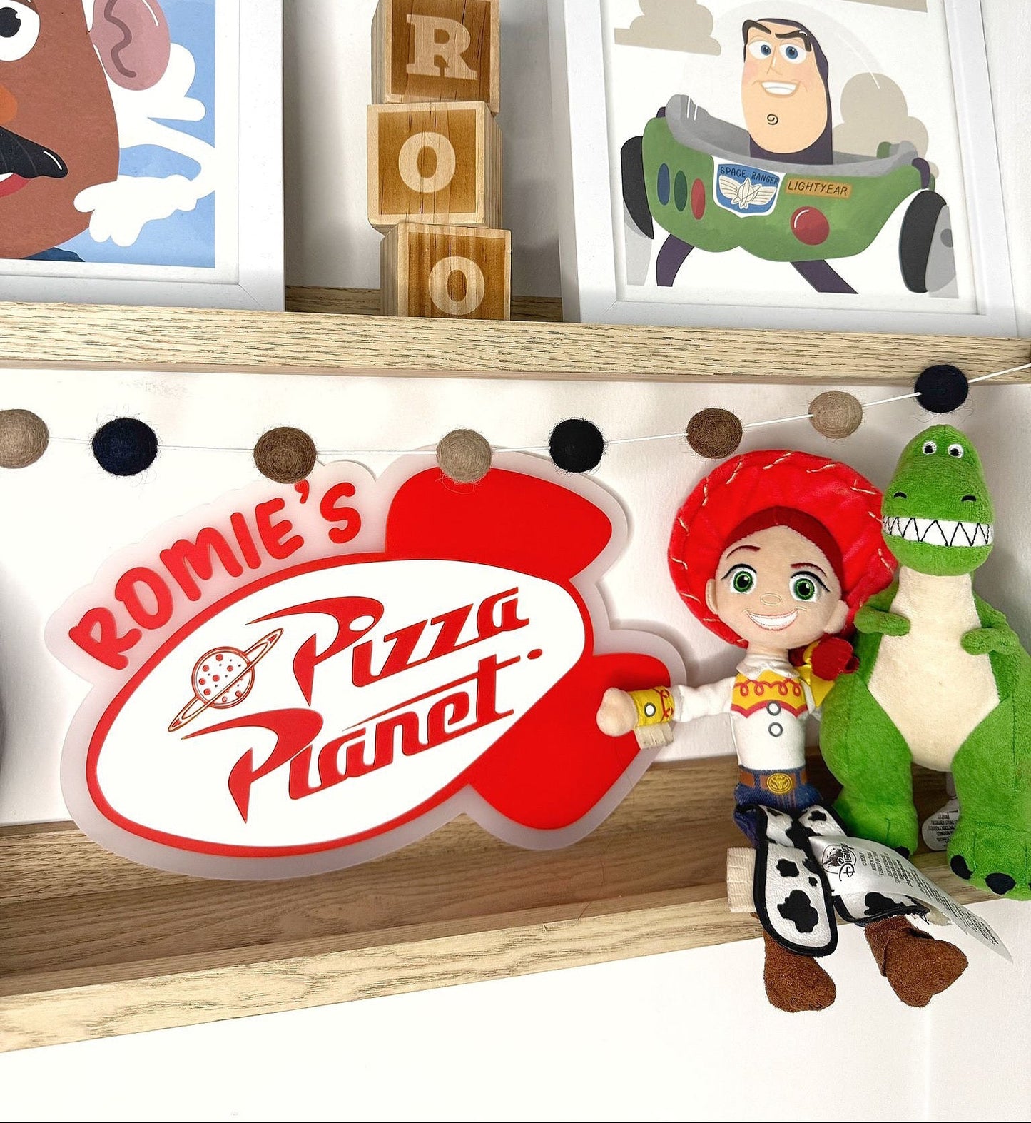 Shelf with 'Rommie's Pizza Planet' sign, toy figures, and framed pictures of cartoon characters.